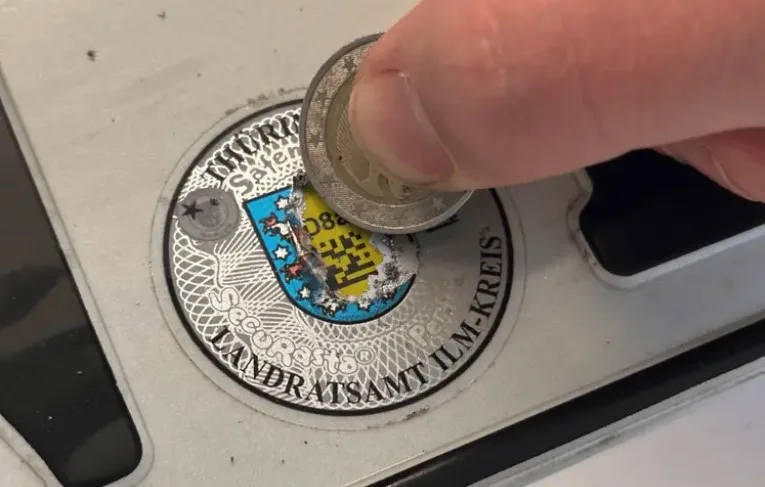 Nahaufnahme einer Stempelplakette beim vorsichtigen Freirubbeln mit einer Münze
